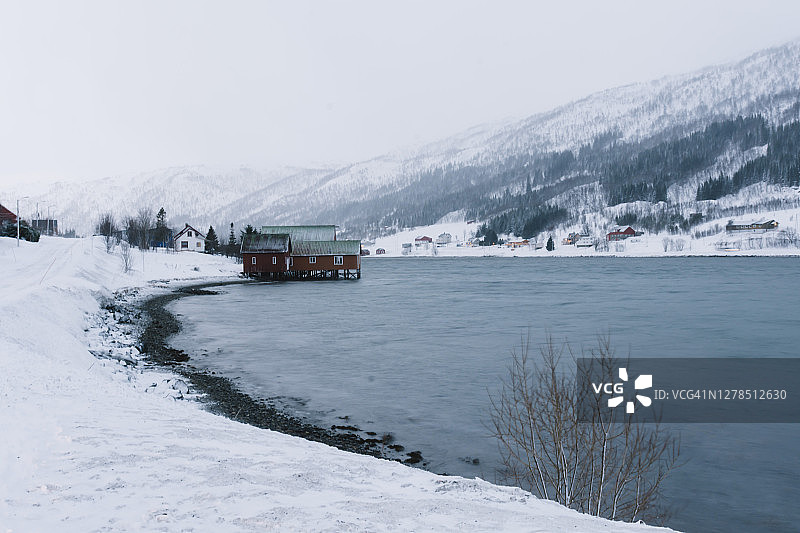 冬季极夜期间挪威北部Kvaløya俯瞰湖泊和峡湾的红色渔屋图片素材