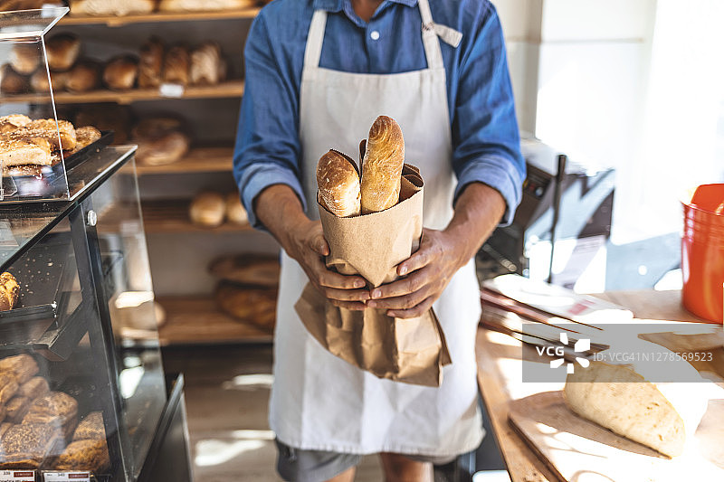 自豪的男性面包店工人在面包店展示面包图片素材