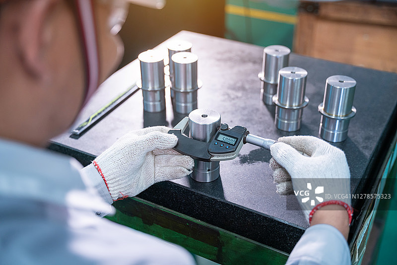 亚洲技术员穿安全服在工业厂房用数字千分尺检查花岗岩表面的尺寸图片素材