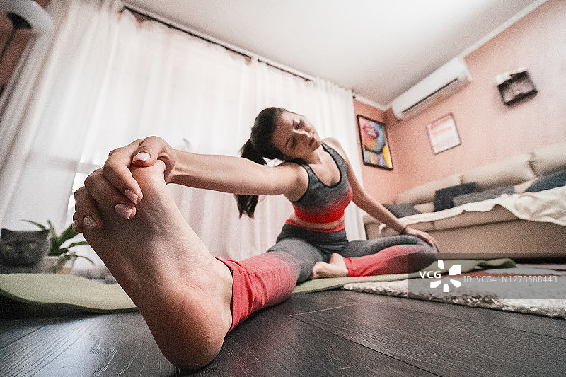 年轻女子在家做瑜伽放松练习，在客厅锻炼，居家保持体形，COVID-19疫情持续图片素材