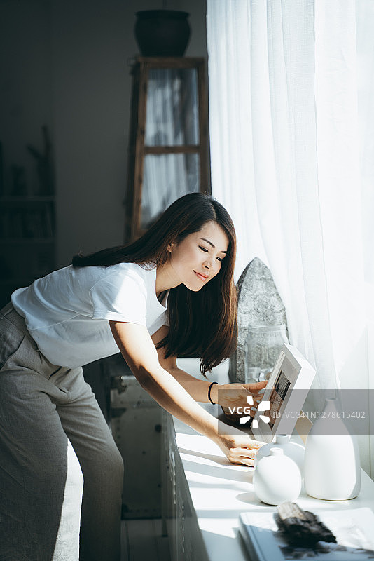 亚洲年轻女人在家整理相框花瓶图片素材