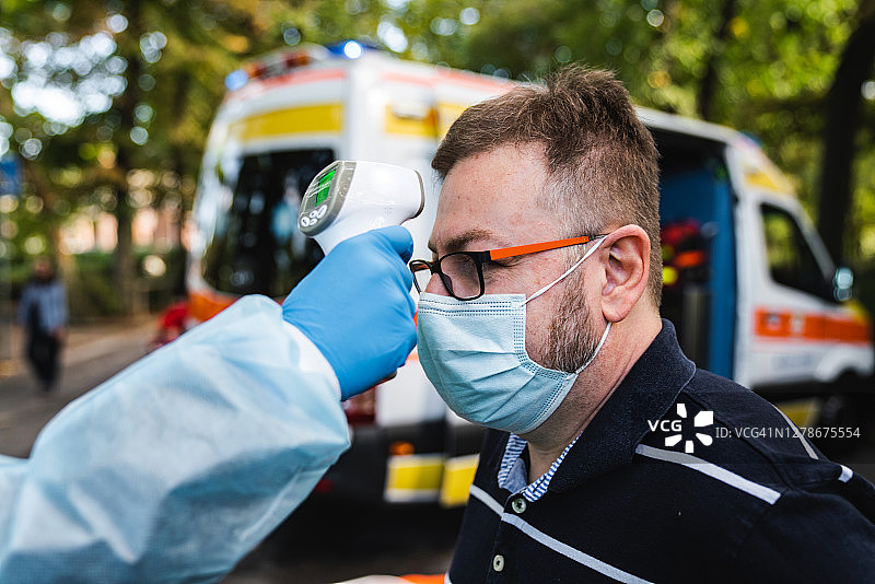 穿防护服的医生为一名男子测量体温图片素材