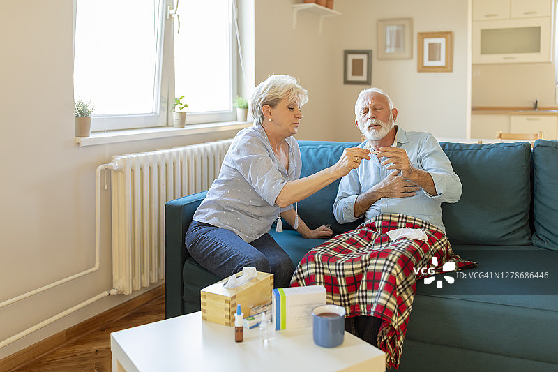 一位老人很高兴有护理人员在他身边。患有病毒和高烧的老年男子很高兴得到他细心的妻子的照顾。病毒COVID-19。图片素材