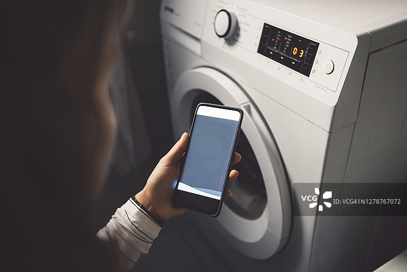 用手机查看洗衣机能源使用情况的女人图片素材