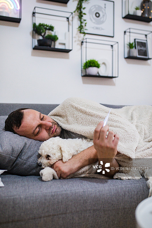 生病的男人在床上用体温计检查体温图片素材