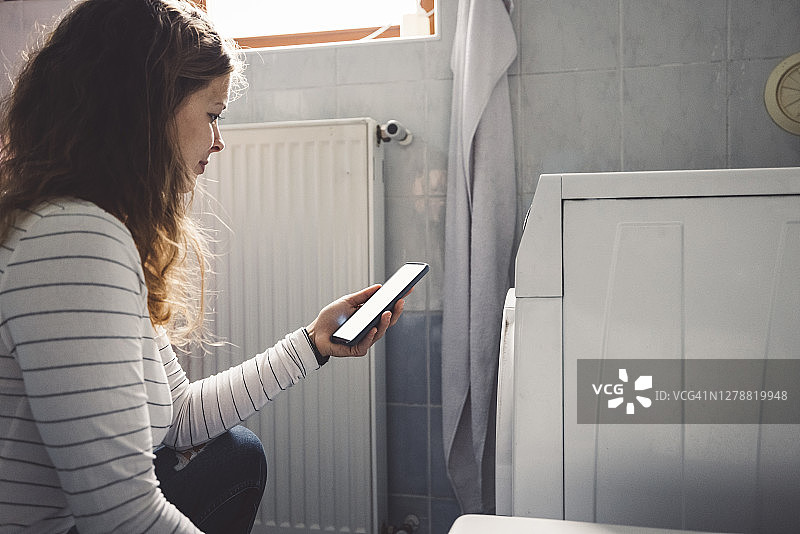 用手机查看洗衣机能源使用情况的女人图片素材