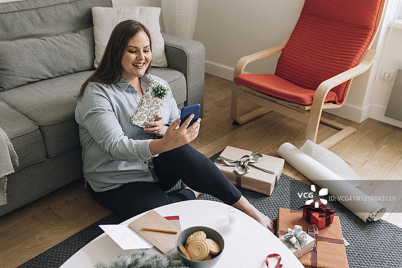 快乐的大码女性在视频通话中向某人展示包装好的圣诞礼物，新常态概念图片素材