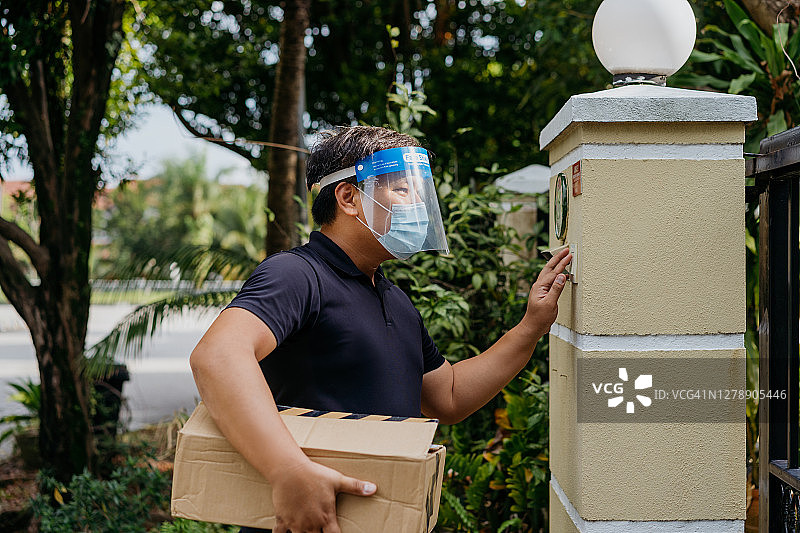 亚洲快递员手持包裹按门铃图片素材