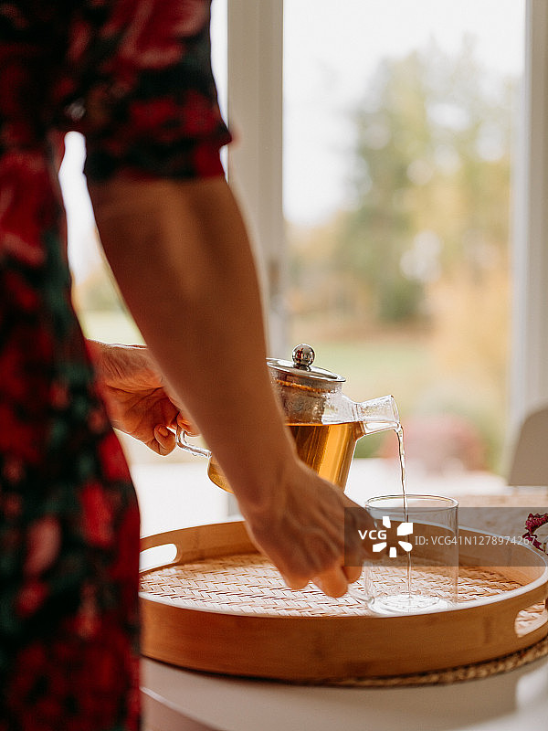 女人在茶道中将新鲜冲泡的茶倒入玻璃杯和茶壶图片素材