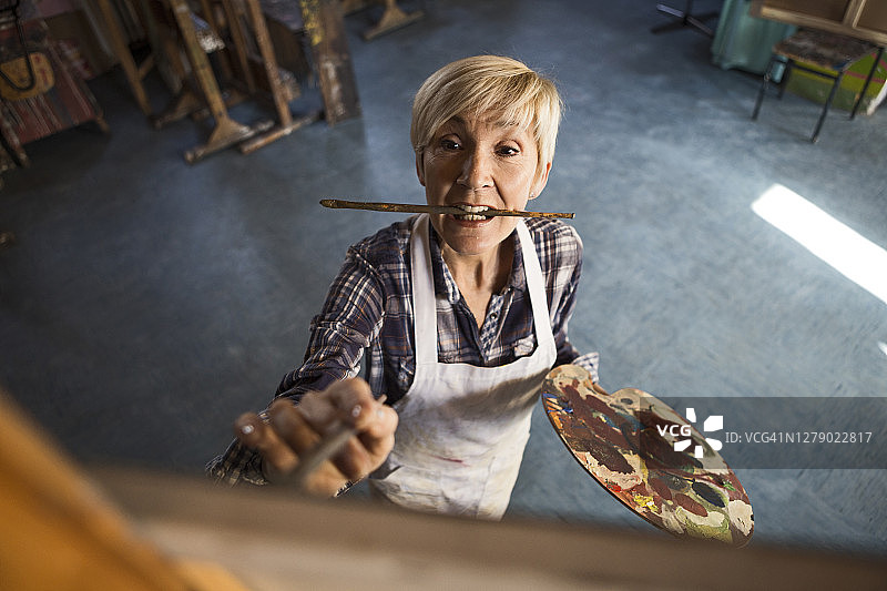 年长的女人在工作室里用画笔在画布上绘画图片素材