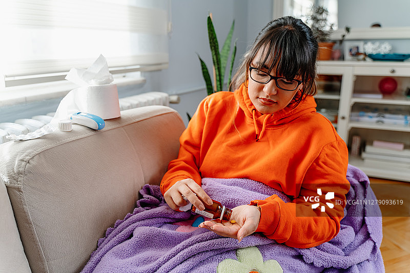 疾病，季节性病毒问题概念。女人躺在沙发上生病，看着温度计上的温度。生病的女人发高烧躺在床上。感冒和偏头痛图片素材
