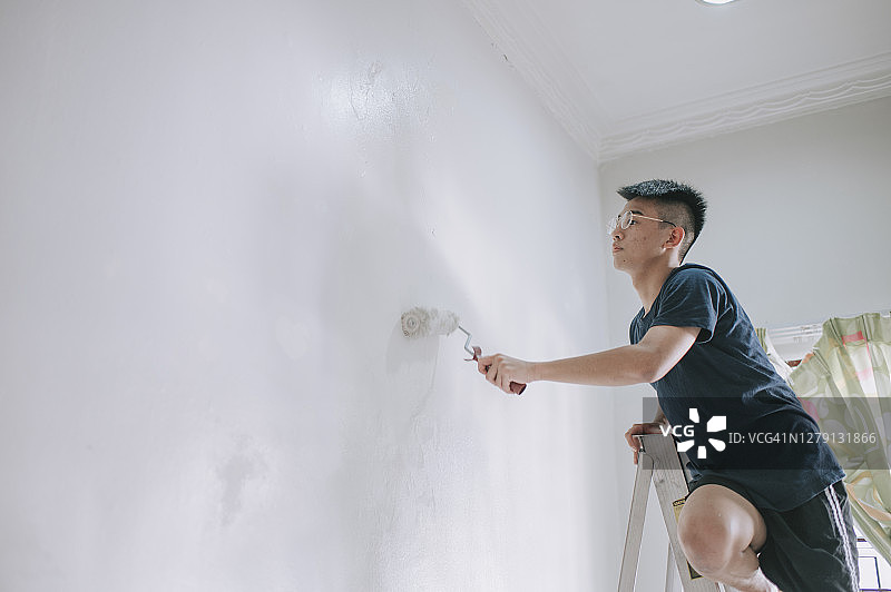 日落时分，一位亚洲男孩正在粉刷卧室，公寓翻新图片素材