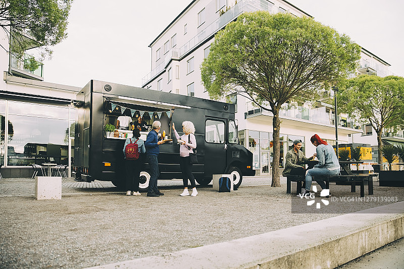 在城市里，男性和女性顾客在商务车附近等待印度食物图片素材