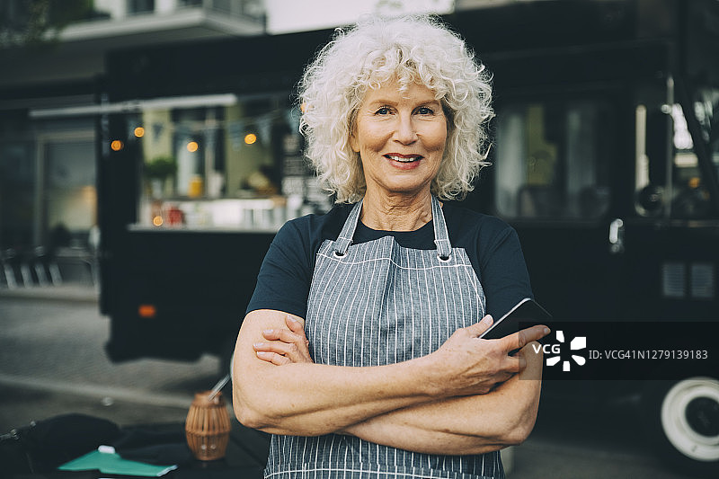拿着智能手机站在城市餐车前的老年店主肖像图片素材