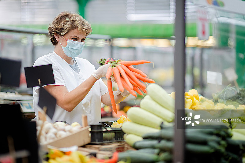 戴口罩的女人在食品市场卖胡萝卜图片素材