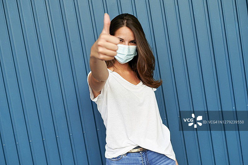 佩戴防病毒口罩，做出胜利手势的微笑女性肖像图片素材