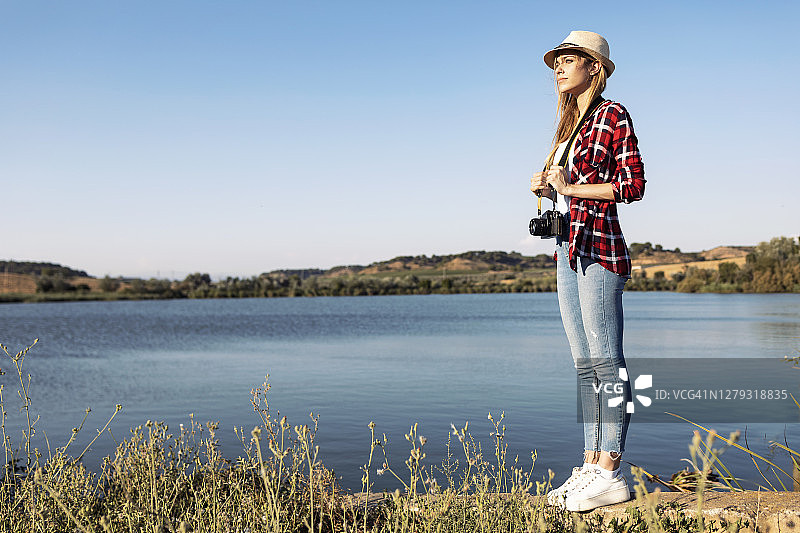 站在挡土墙上，拿着相机的年轻女人，背景是晴朗的天空图片素材