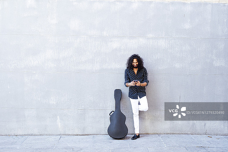 男人靠在水泥墙上用手机弹吉他图片素材