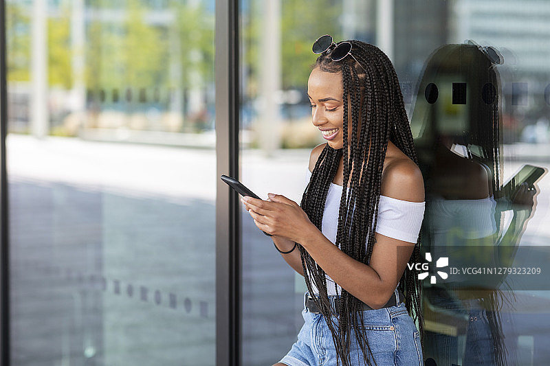 倚靠在城市玻璃墙边用手机的女人图片素材