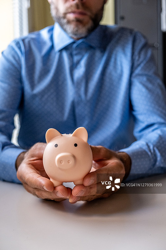 穿着蓝色衬衫，双手捧着小猪存钱罐的男人图片素材