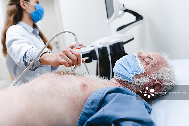 特写照片：老年患者戴着口罩，女医生戴着口罩进行胸部超声检查图片素材
