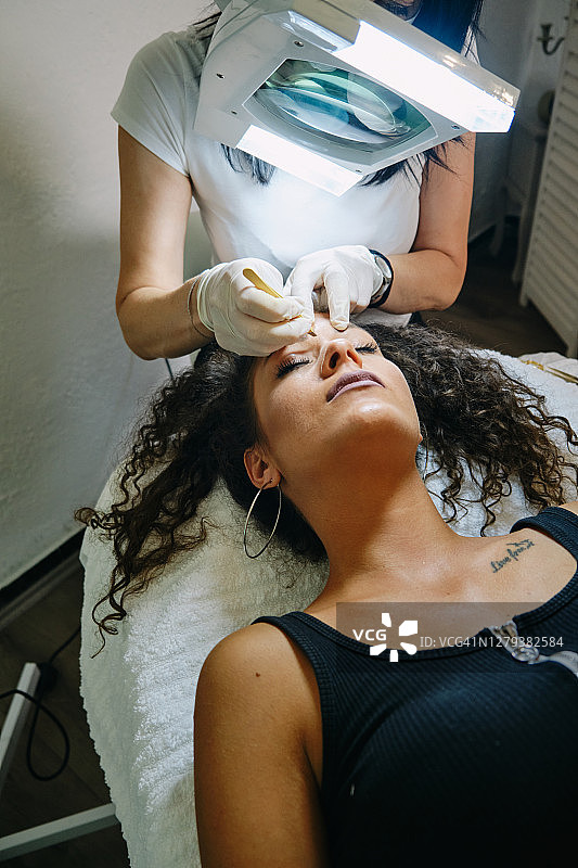 美容师在美容院用眉毛镊子为年轻女顾客修眉图片素材