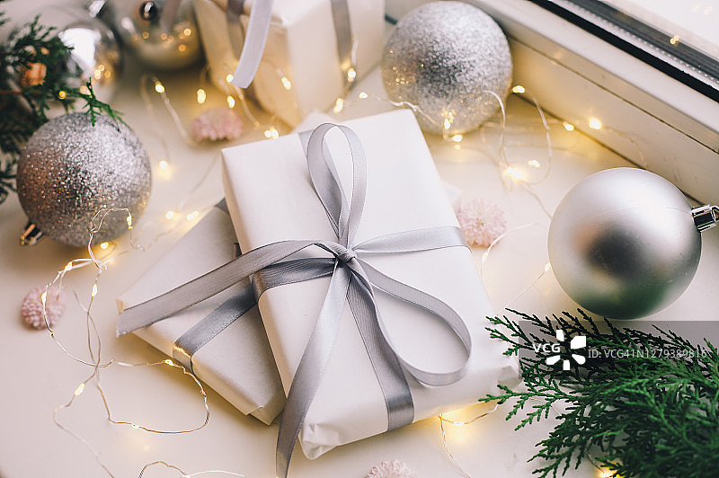 白色背景上的自制圣诞礼盒、银色丝带、装饰品、冷杉树和串灯图片素材