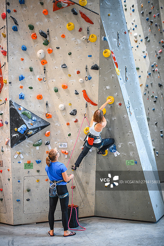年轻的女运动员沿着攀岩墙向上攀登图片素材