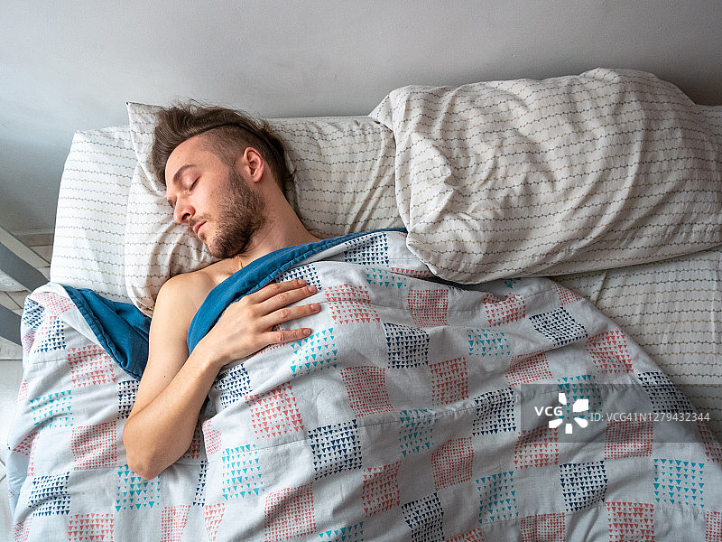 早上，年轻的白人男子在他的床上睡觉图片素材