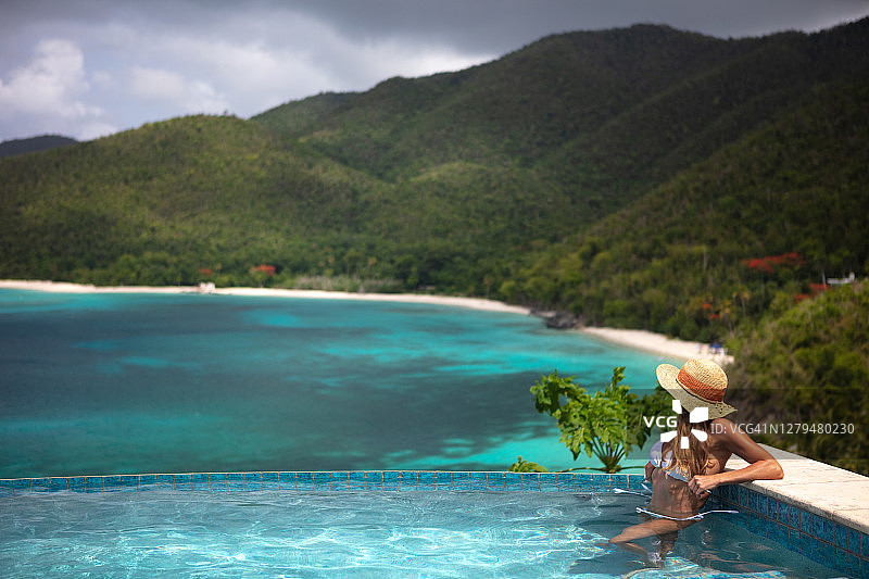 在豪华别墅的无边泳池中放松的迷人女人图片素材