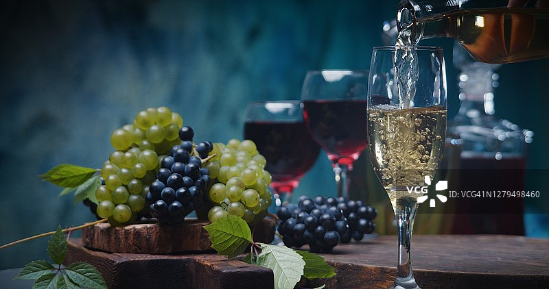 在蓝色背景下倒入白葡萄酒，搭配红色和白色葡萄以及葡萄酒瓶图片素材