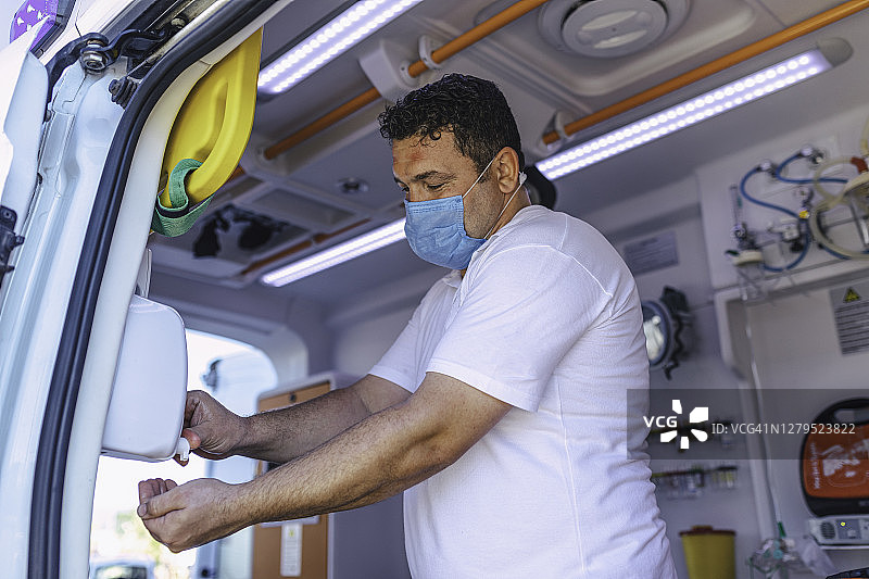 疫情期间，戴着口罩的男性护理人员在救护车内对手进行消毒图片素材