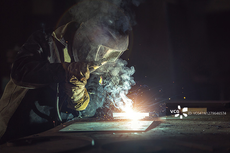 建筑工地中佩戴安全面罩和手套的产业工人焊接钢结构，建筑行业安全概念图片素材