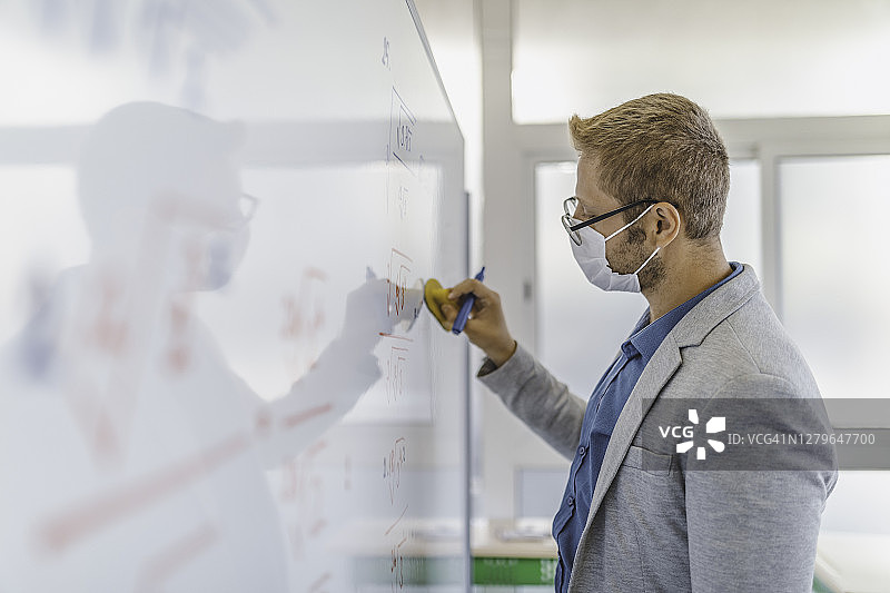 年轻男老师戴着口罩在教室白板上写字图片素材