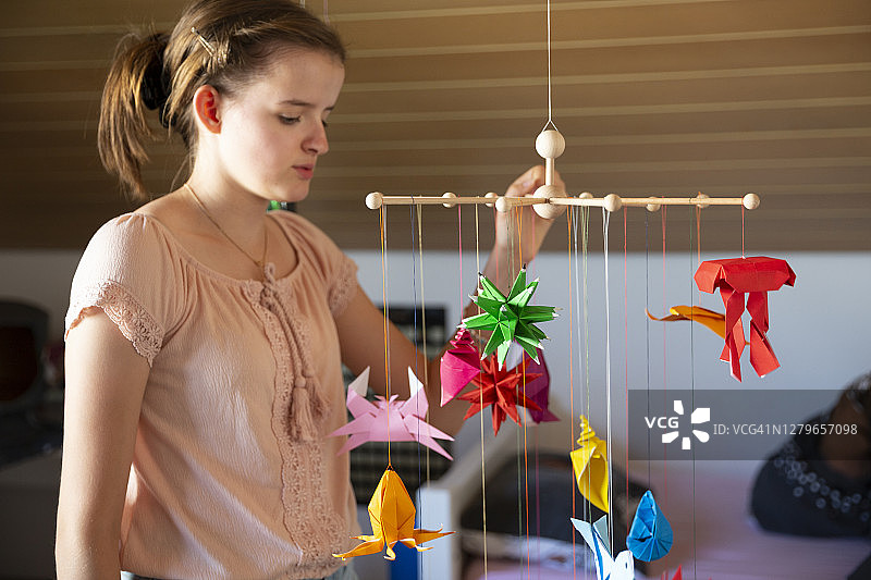 在婴儿床边玩自制彩色折纸挂饰的少女图片素材