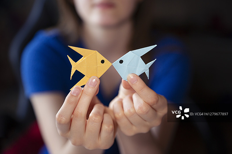 青少年拿着用彩色纸制作的自制双鱼折纸雕塑图片素材