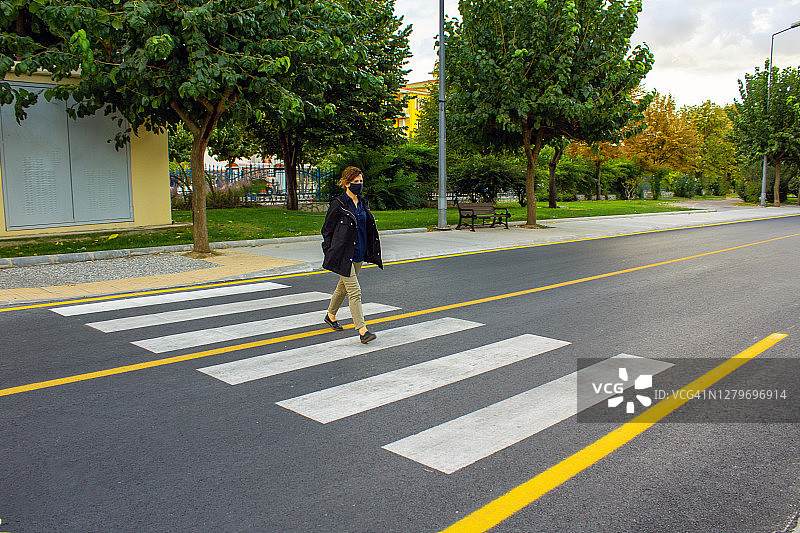 疫情期间，年轻女人戴着防护口罩在十字路口过马路图片素材