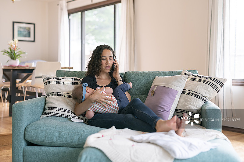 千禧一代母亲在家一边哺乳一边用手机通话图片素材