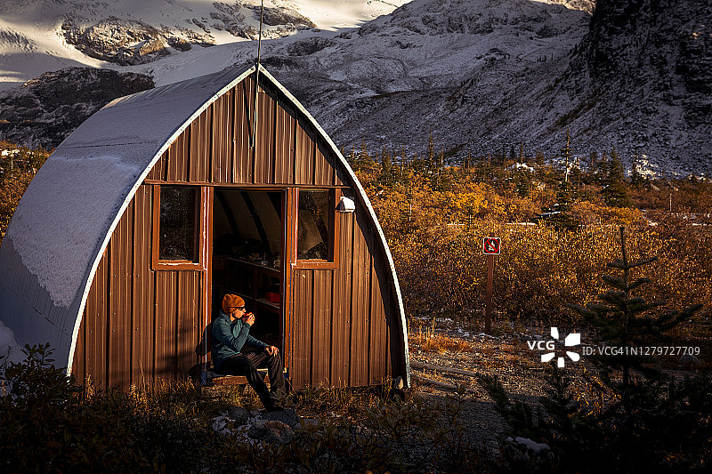 男人坐在乡村小屋入口处喝着热饮，欣赏日落图片素材