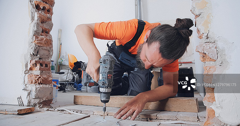 男人在新家铺地板，用钻拧紧木板图片素材