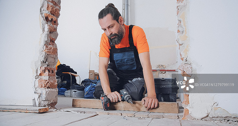 男人在新家铺地板，用钻拧紧木板图片素材