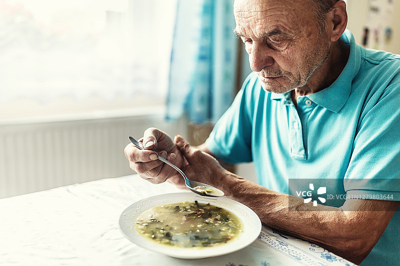 患有帕金森病的老年人扶着手臂，努力喝汤图片素材