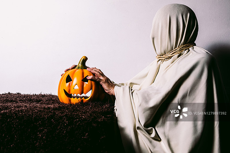 白色墙壁上手持万圣节南瓜的妖怪图片素材