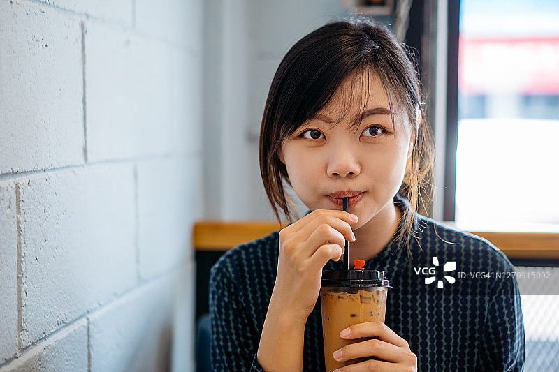 在咖啡馆里享用冰奶茶的年轻亚洲女性图片素材