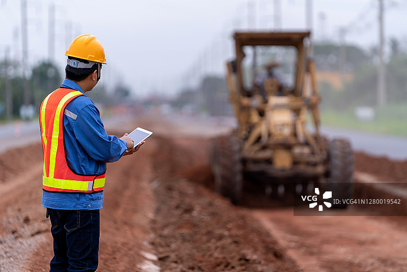 土木工程师戴着头盔控制平地机，改善道路基础，平地机在道路施工现场进行土木工程施工图片素材