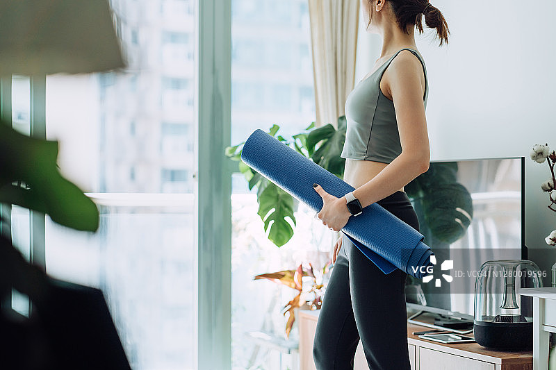 自信而坚定的年轻亚洲运动女性拿着瑜伽垫，准备在明媚的早晨在家练习瑜伽。健身、健康和健康生活理念图片素材