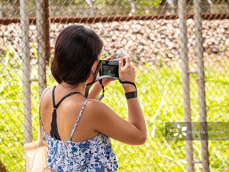 身穿白色连衣裙的年轻西班牙裔女人用相机拍照图片素材