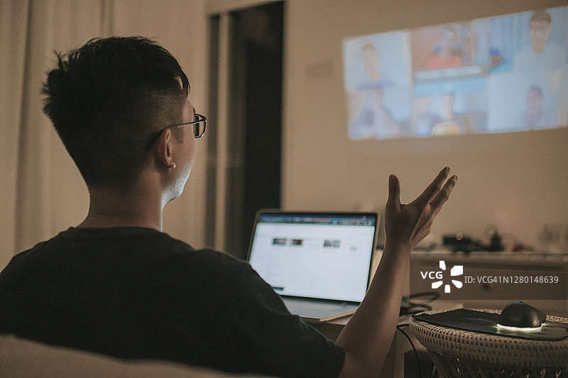 中国男性在家使用笔记本电脑和投影仪屏幕进行视频会议图片素材