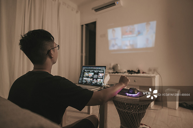 中国男性在家使用笔记本电脑和投影仪屏幕进行视频会议图片素材