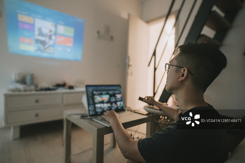 中国男性在家使用笔记本电脑和投影仪屏幕进行视频会议图片素材